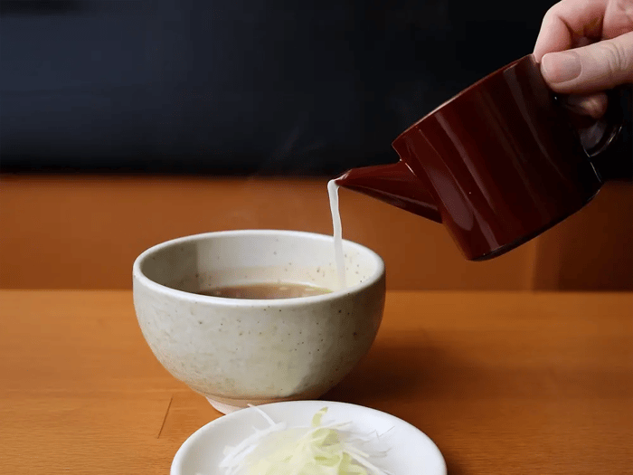 つけ麺の食後、つけダレに熱い割りスープを注いでスープ割を楽しむ様子。横には白髪ねぎが添えられている。