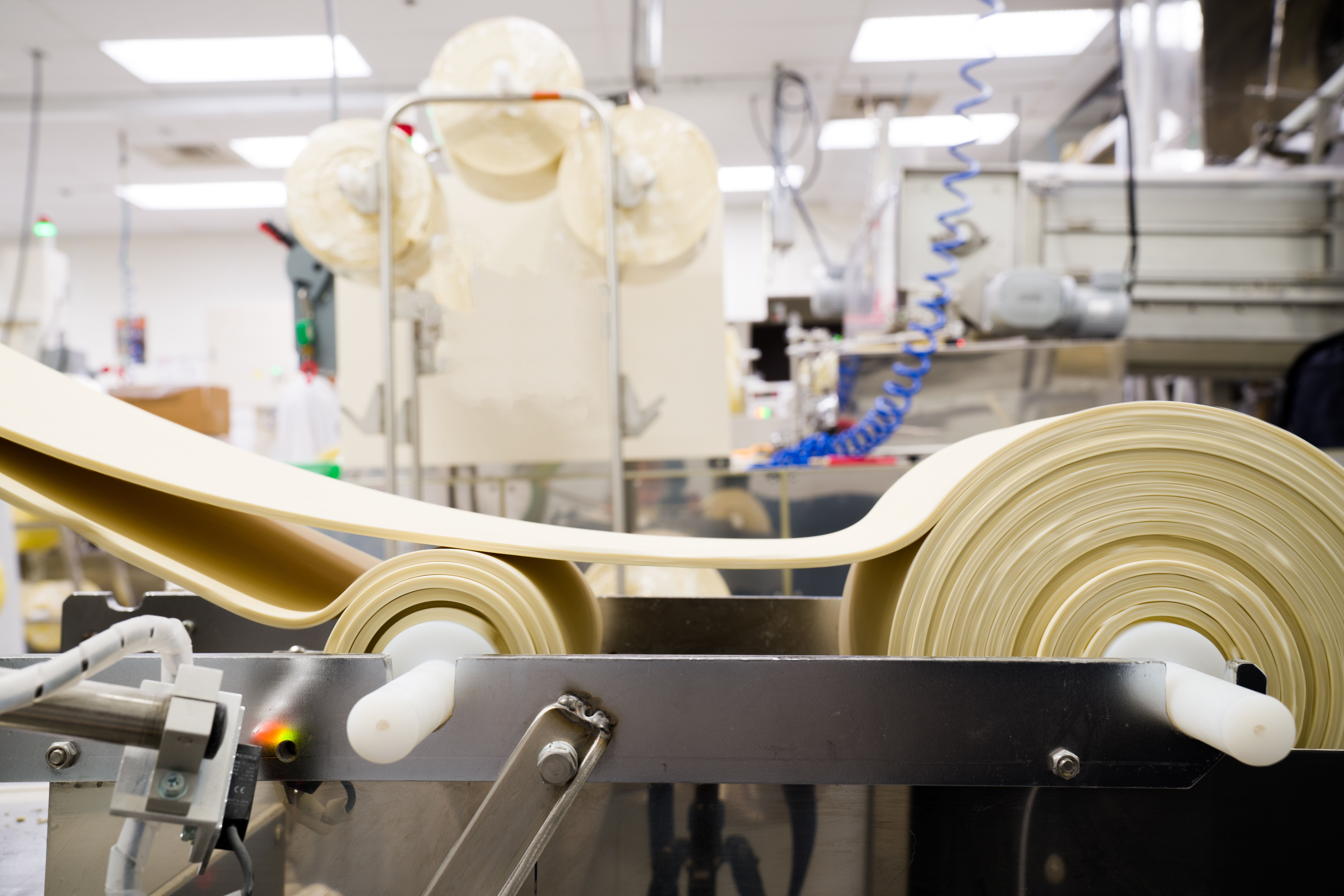 Ramen noodle dough sheets moving through rollers during noodle production.